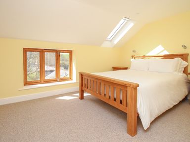 A bedroom with a wooden bed and side tables under a slanted ceiling with skylight windows at The Stables Burton Bradstock
