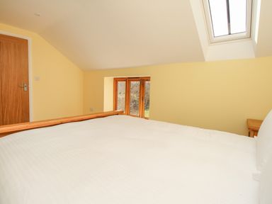 A bedroom with a large bed wooden door small window skylight and a wooden nightstand at The Stables Burton Bradstock