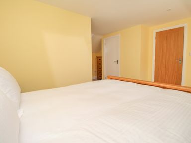 A bedroom with a bed with white bedding two doors and a wooden chest of drawers at The Stables Burton Bradstock