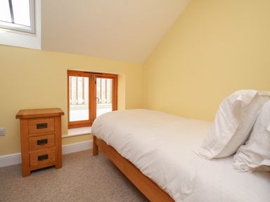 A small bedroom with a wooden bed and white bedding next to a wooden bedside table and a window at The Stables Burton Bradstock