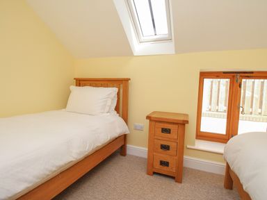 A bedroom with two single beds and a wooden bedside table under a skylight at The Stables Burton Bradstock