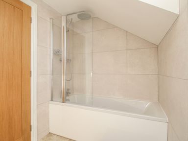 A bathroom with a bathtub shower combination and tiled walls at The Stables Burton Bradstock