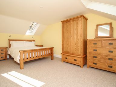 A bedroom with a wooden bed frame white bedding wooden wardrobes dresser with mirror and nightstands at The Stables Burton Bradstock