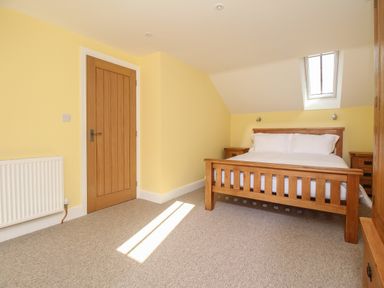 A bedroom with a wooden bed and twin bedside tables next to a wooden door and a skylight window at The Stables Burton Bradstock