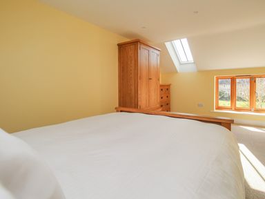 A bedroom with a bed a wooden wardrobe a chest of drawers a skylight and a window at The Stables Burton Bradstock