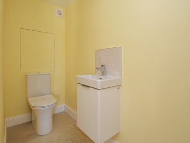 A bathroom with a toilet and a wall-mounted sink at The Stables Burton Bradstock