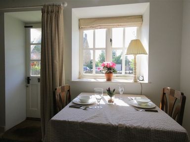 A dining table set for two by a window with a flower pot and lamp at Noel Cottage in Chipping Campden