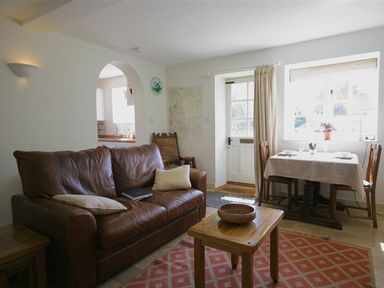 A living room with a brown leather sofa wooden table and a dining table by the window at Noel Cottage in Chipping Campden