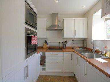 A kitchen with white cabinets wooden countertops a built in oven and microwave a sink under a window and kitchen utensils at Noel Cottage in Chipping Campden