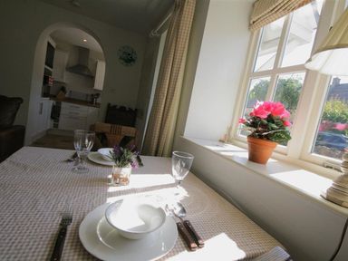 A dining table set with plates and glasses next to a window with a potted plant in a kitchen at Noel Cottage in Chipping Campden