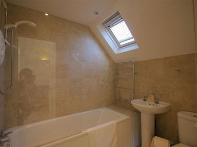 A bathroom with a bathtub shower combination sink toilet window and towel rail at Noel Cottage in Chipping Campden