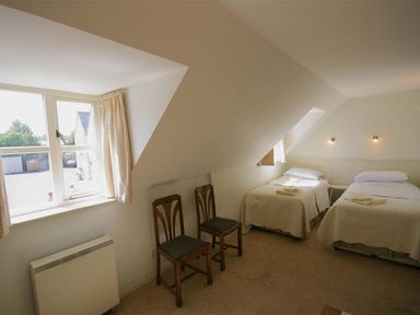 A bedroom with two single beds two wooden chairs and a window with curtains at Noel Cottage in Chipping Campden