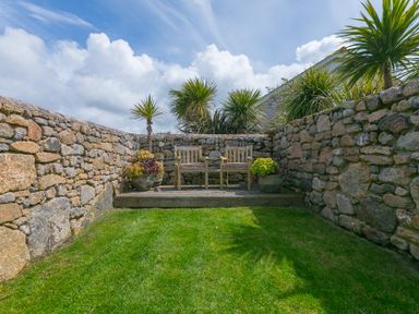 A garden with a stone wall and wooden benches at Scilly Stack in Penzance