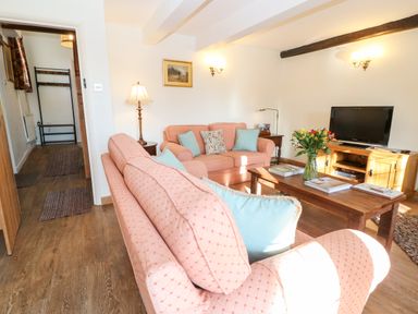 A living room with two pink sofas and a wooden coffee table with flowers and magazines at Cowfair Cottage in Chipping Campden
