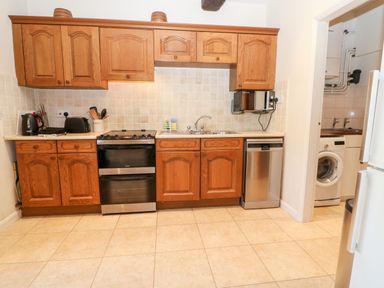A kitchen with wooden cabinets a stove a sink dishwasher microwave and washing machine at Cowfair Cottage in Chipping Campden