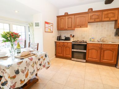 A kitchen with wooden cabinets a dining table with a bread loaf and flowers at Cowfair Cottage in Chipping Campden