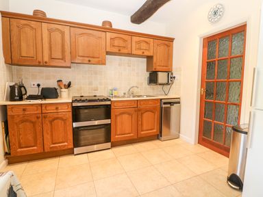 A kitchen with wooden cabinets a stove a sink a microwave a dishwasher and a glass-paneled door at Cowfair Cottage in Chipping Campden