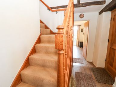 A wooden staircase with carpeted steps in a hallway with wooden doors and rugs at Cowfair Cottage in Chipping Campden