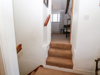 Carpeted stairs leading to a room with a window a desk chair and curtains at Cowfair Cottage in Chipping Campden
