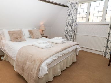 A bedroom with a double bed two pillows bedside table with lamp and window with floral curtains at Cowfair Cottage in Chipping Campden
