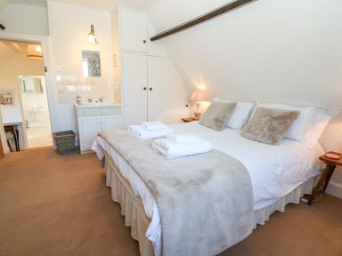 A bedroom with a double bed towels on the bed bedside tables lamps a sink and a doorway to an adjoining bathroom at Cowfair Cottage in Chipping Campden