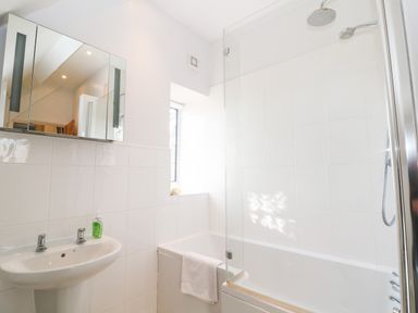 A bathroom with a sink and mirror cabinet and a bathtub with a shower at Cowfair Cottage in Chipping Campden