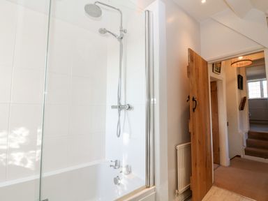 A bathroom with a bathtub and shower next to a wooden door leading to a hallway at Cowfair Cottage in Chipping Campden