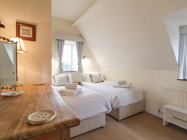 A bedroom with two single beds with white bedding a wooden desk and a window with curtains at Cowfair Cottage in Chipping Campden