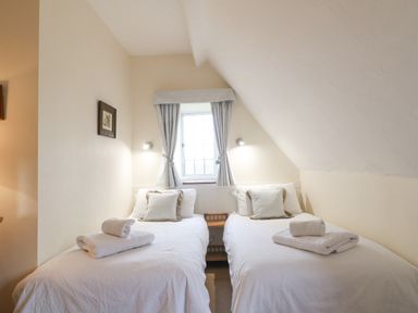 A bedroom with two single beds and a window with curtains at Cowfair Cottage in Chipping Campden