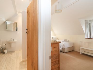 A bedroom with a bed, wooden dresser, window with curtains and a bathroom with a sink, toilet and mirror at Cowfair Cottage in Chipping Campden