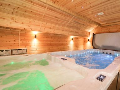 A hot tub with green and blue lighting inside a wooden room at Tynewydd Fields in Cross Inn