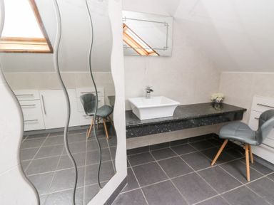 A bathroom with a sink, mirror, and chair at Tynewydd Fields, Cross Inn