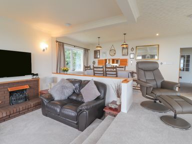 A living room with a leather sofa, recliner chair, brick fireplace, dining table, and wall mirrors at Aelwyd Y Don in Tresaith