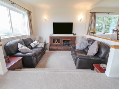 A sunken living room with two leather sofas facing a brick fireplace and flat screen TV at Aelwyd Y Don in Tresaith