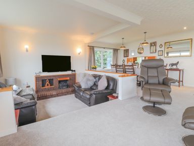 A living room with leather sofas a TV above a fireplace and a dining area with wooden chairs at Aelwyd Y Don in Tresaith