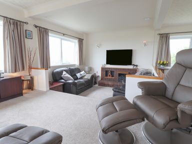 A living room with leather sofas a recliner chair a wall mounted TV and a brick fireplace at Aelwyd Y Don in Tresaith