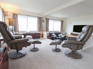 A living room with recliner chairs a sofa a TV and windows with curtains at Aelwyd Y Don in Tresaith