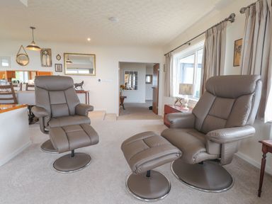 A living room with two gray leather recliners and a footstool near a window with curtains at Aelwyd Y Don in Tresaith