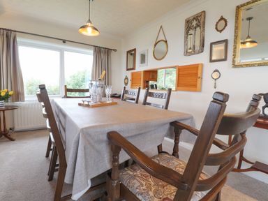A dining room with a table covered with a cloth and wooden chairs with mirrors on the wall at Aelwyd Y Don in Tresaith