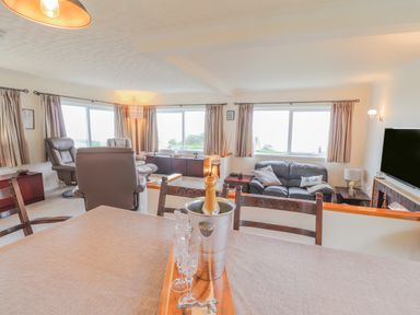 A living room with leather armchairs a sofa a TV and a dining table with a champagne bottle at Aelwyd Y Don in Tresaith