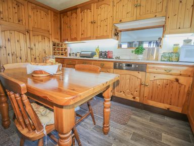 A kitchen with wooden cabinets a wooden table and chairs and various appliances at Aelwyd Y Don in Tresaith
