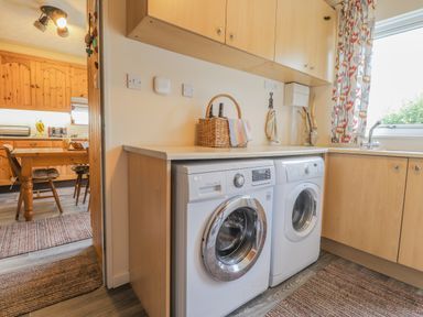 A utility room with washing machines and a basket on the counter next to a sink and window at Aelwyd Y Don in Tresaith