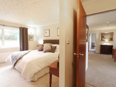 A bedroom with a bed pillows and curtains next to an open door showing a room with dressers and a chair at Aelwyd Y Don in Tresaith