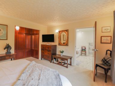 A bedroom with wooden furniture a mounted television an open door to a bathroom at Aelwyd Y Don in Tresaith