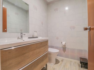 A bathroom with a wooden vanity and mirror next to a toilet and tiled walls at Aelwyd Y Don in Tresaith
