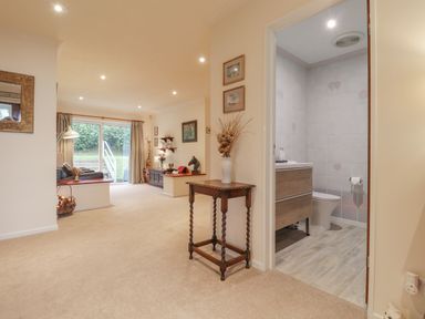 A hallway with a small wooden table and a vase with dried flowers next to a bathroom and a living room with sliding glass doors at Aelwyd Y Don in Tresaith
