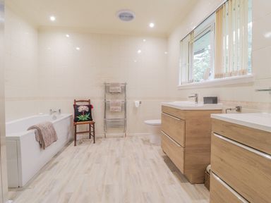 A bathroom with a bathtub a wooden chair a towel rack two sinks and a window at Aelwyd Y Don in Tresaith