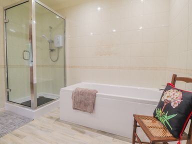 A bathroom with a shower enclosure bathtub a wooden chair with a floral cushion and a towel at Aelwyd Y Don in Tresaith