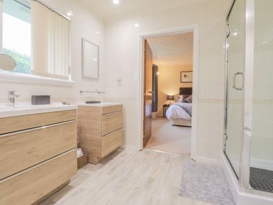 A bathroom with wooden cabinets a sink a shower and a view into a bedroom at Aelwyd Y Don in Tresaith