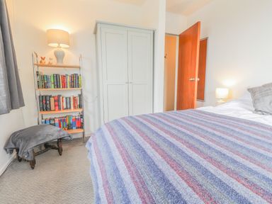 A bedroom with a bed covered with a striped blanket a bookshelf a wardrobe an open door and two lamps at Aelwyd Y Don in Tresaith
